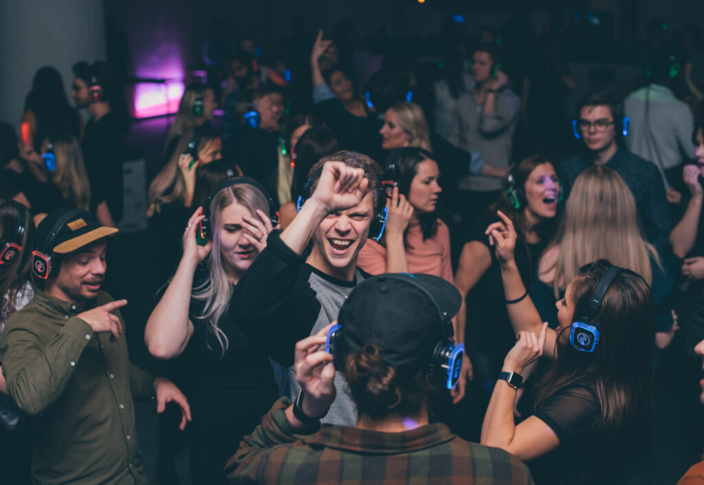 Energetic audience dances with headphones in colorful club lights.